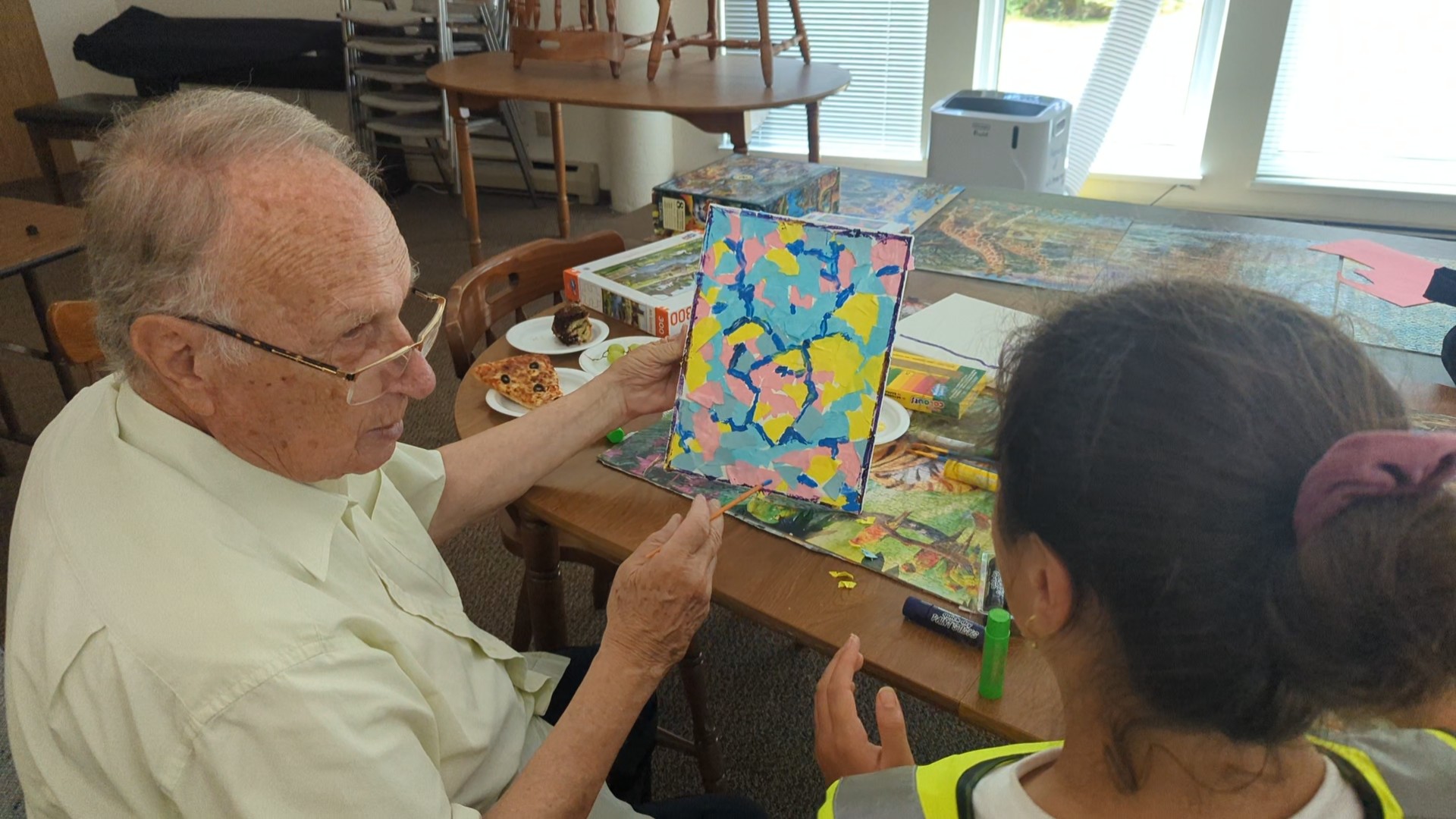 A senior man provides some feedback to a participant as they look over her very colourful artwork.