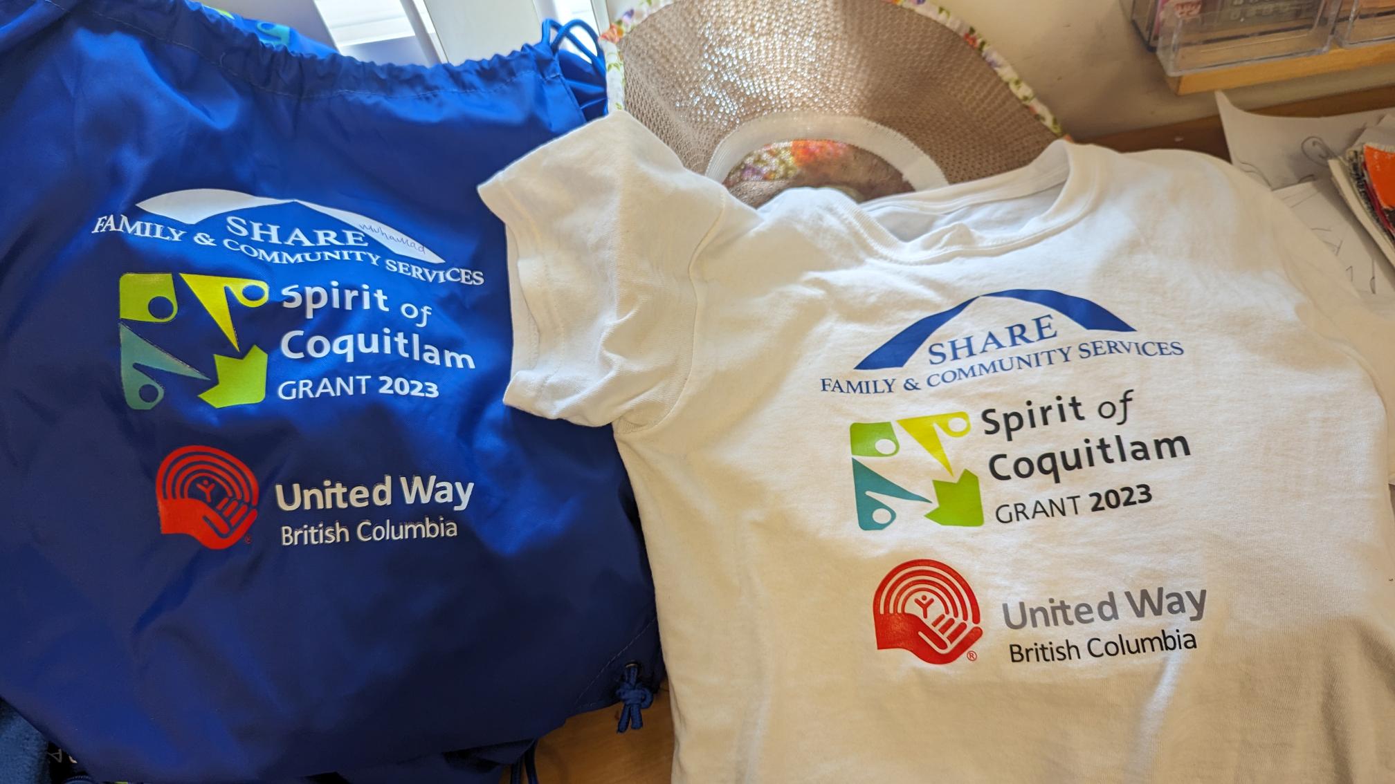 Photo of a blue backpack and a white t-shirt with the logos of SHARE, Spirit of Coquitlam grant, and United Way of BC.  Each child was presented with one to keep.
